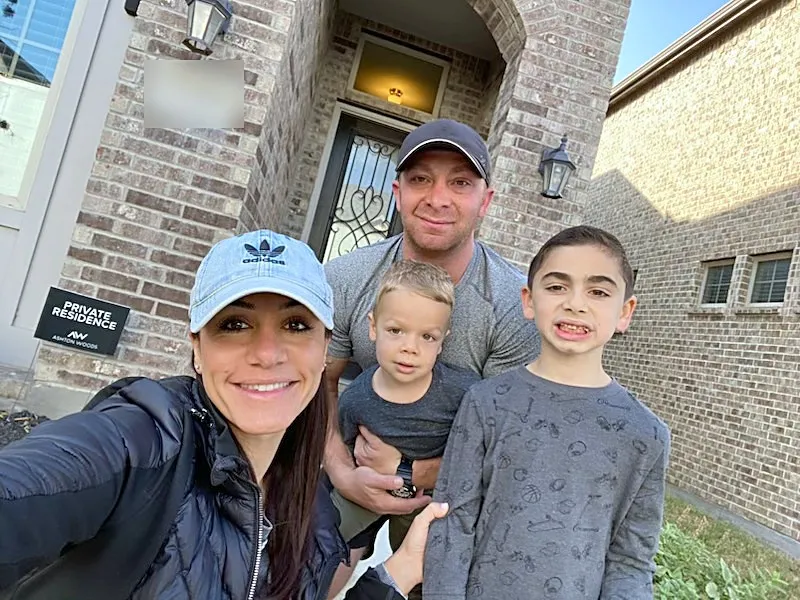 A family of four, two parents and two boys, outside a brick home
