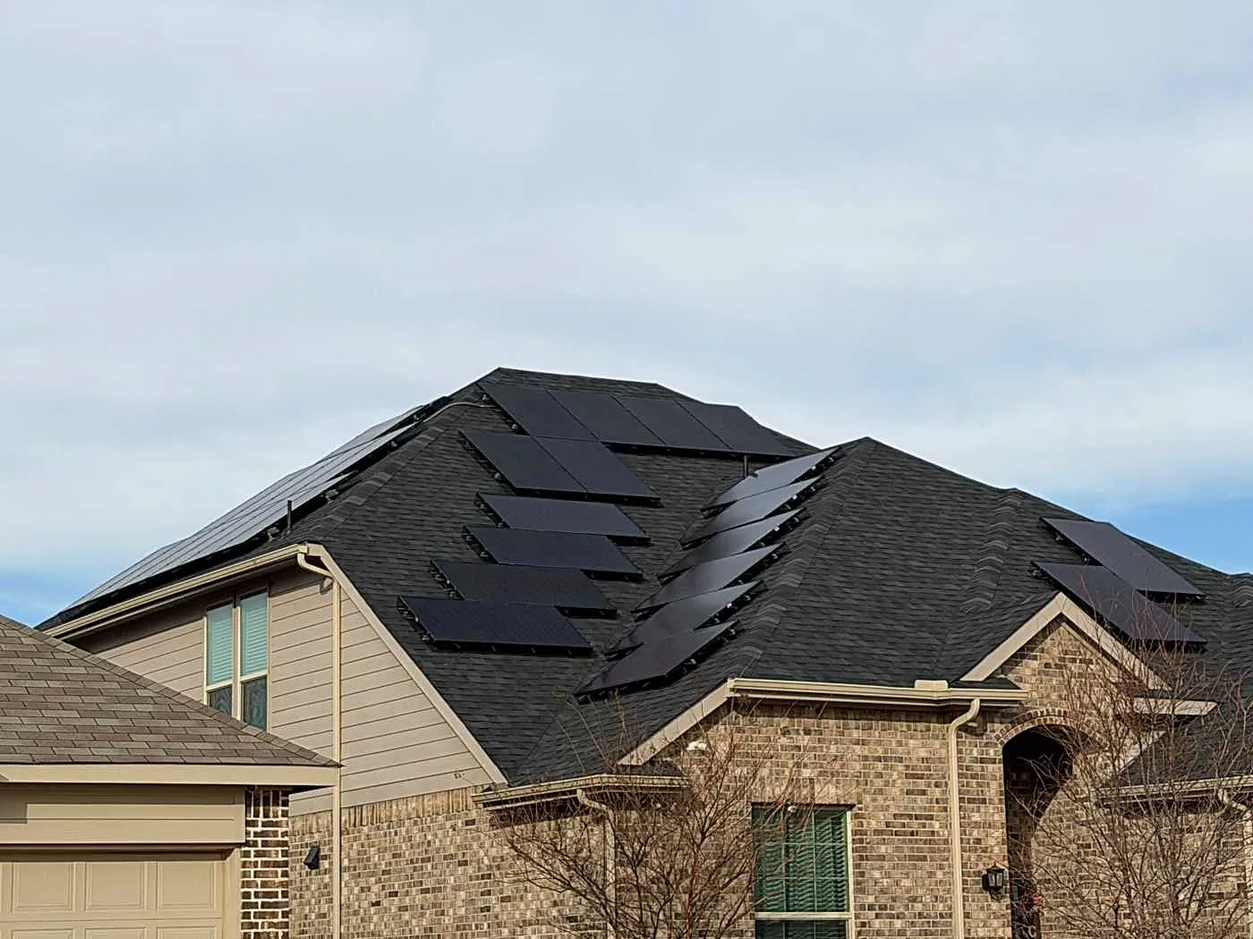 Solar panels on a dark shingle roof over a brick and siding home