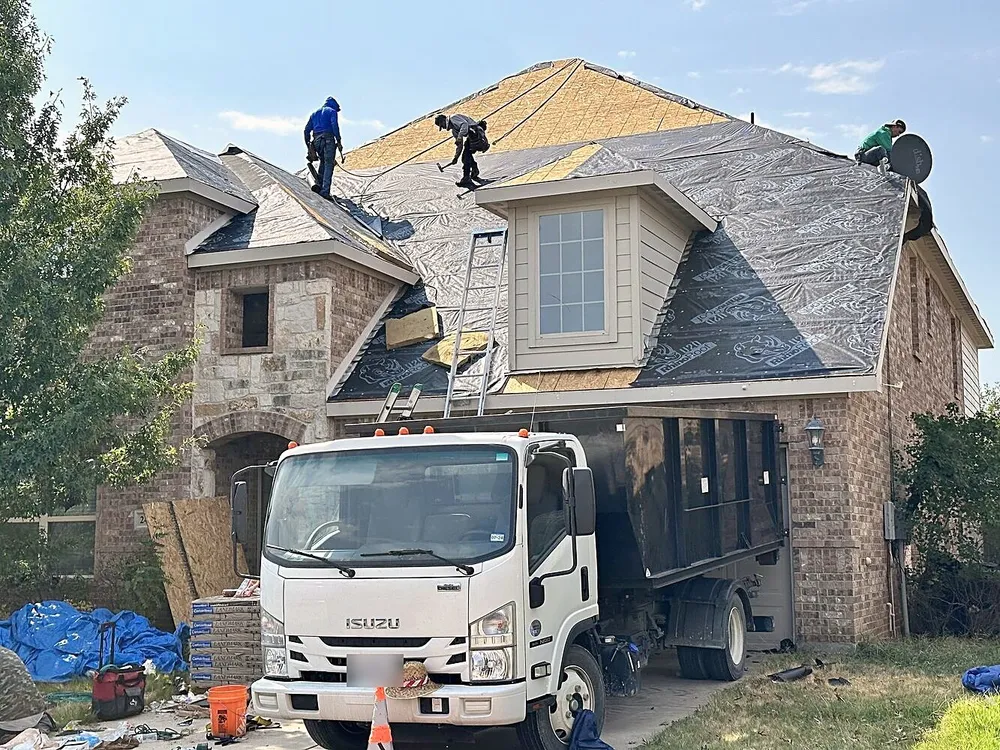Roofers tearing off an old roof down to the decking, with a work truck in the driveway