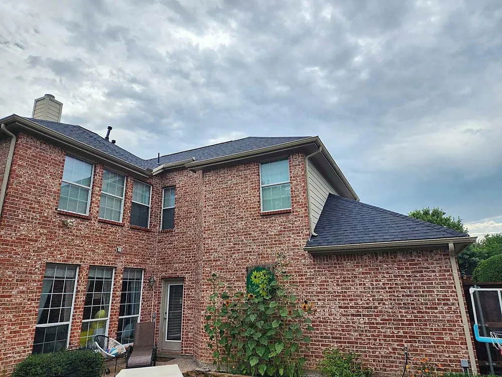The back of a two-story red brick home with a dark shingle roof