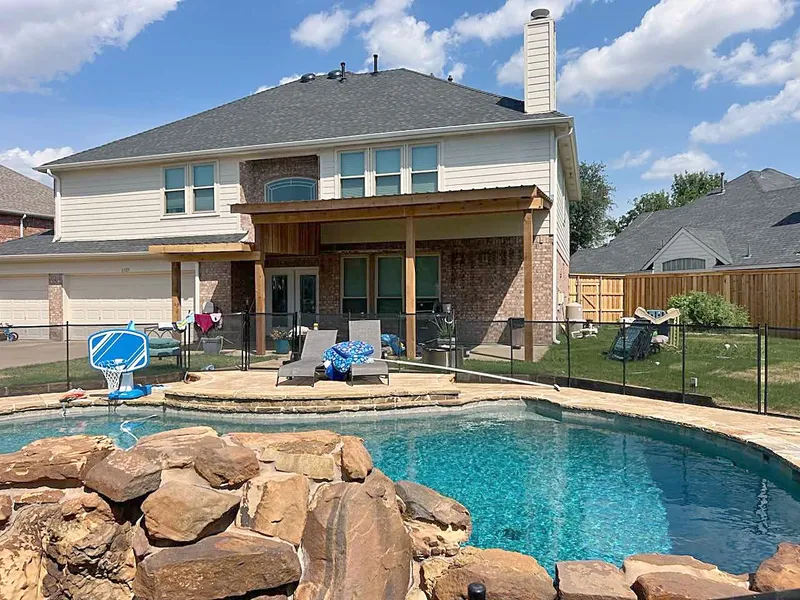 A two-story home with a covered patio and a shingle roof above a backyard pool